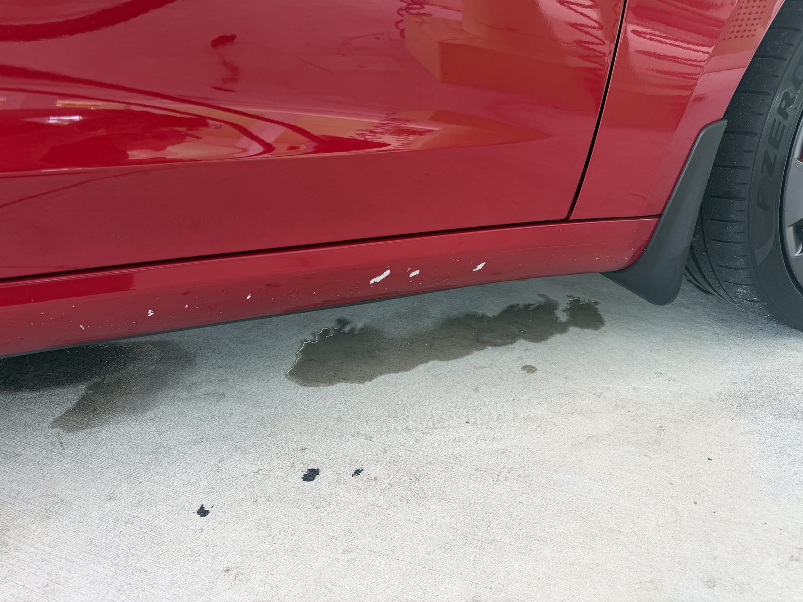 Chipped paint on the lower passenger-side rocker panel of a red Tesla Model 3 after a Kiwi Car Wash visit