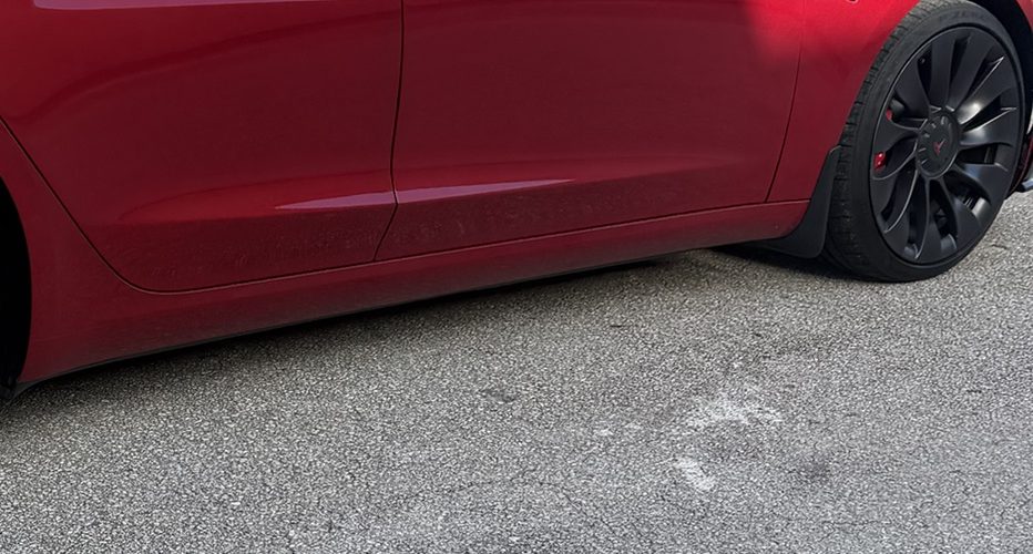 Lower passenger-side rocker panel of a red Tesla Model 3 before the wash, no visible paint chips